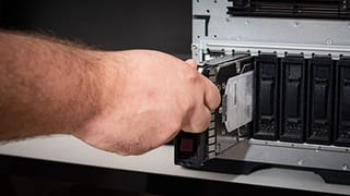 Une main insère un disque dur dans la baie d’un serveur
